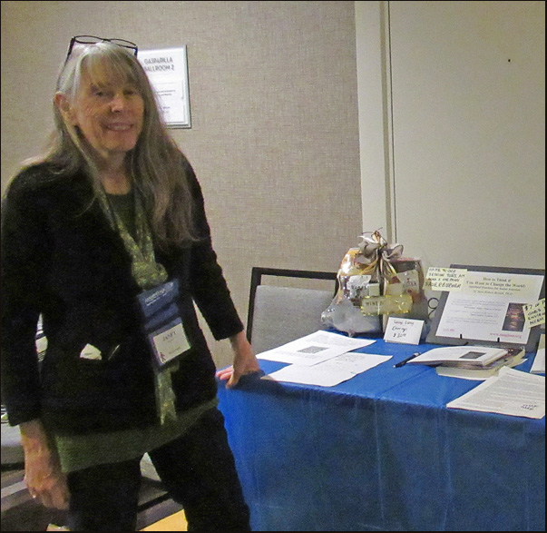 Picture shows Janet Barlow smiling and standing in front of a table with a gift basket and some fliers and poster.